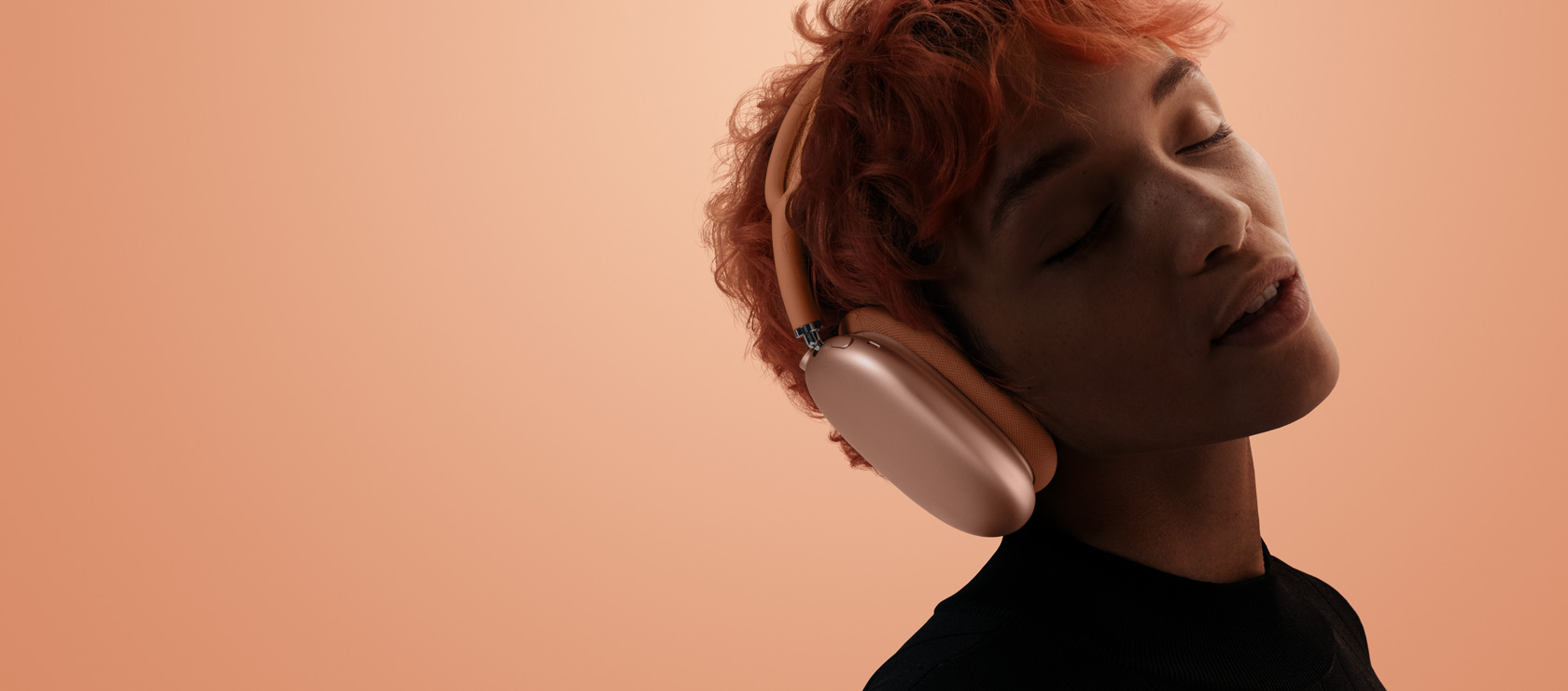 Pessoa com a cabeça inclinada e os olhos fechados usando os AirPods Max 2 na cor laranja sobre um fundo alaranjado
