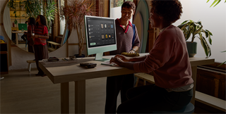 Duas pessoas em uma sala bem iluminada vendo produtos na tela de vidro nano-texture do iMac.