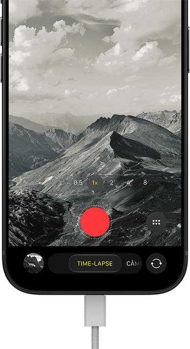 Parte da frente do iPhone 18 Pro mostrando uma paisagem montanhosa, com a sobreposição do modo da câmera no modo time-lapse, com o cabo de energia conectado à porta para recarga