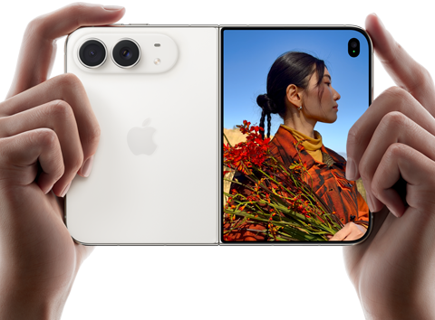 Duas mãos seguram o iPhone Duo na cor branco-estrela aberto na horizontal. O lado esquerdo mostra a câmera dupla Fusion de 48 MP, e o lado direito mostra uma pessoa sendo fotografada na tela externa. A pessoa consegue ver seu rosto enquanto a foto é feita usando o Duo Preview