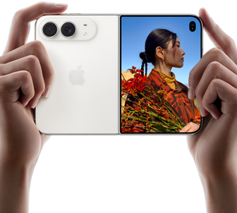 Duas mãos seguram o iPhone Duo na cor branco-estrela aberto na horizontal. O lado esquerdo mostra a câmera dupla Fusion de 48 MP, e o lado direito mostra uma pessoa sendo fotografada na tela externa. A pessoa consegue ver seu rosto enquanto a foto é feita usando o Duo Preview