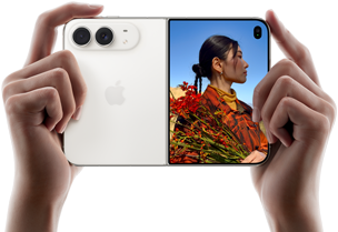 Duas mãos seguram o iPhone Duo na cor branco-estrela aberto na horizontal. O lado esquerdo mostra a câmera dupla Fusion de 48 MP, e o lado direito mostra uma pessoa sendo fotografada na tela externa. A pessoa consegue ver seu rosto enquanto a foto é feita usando o Duo Preview